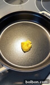 Protein-Packed Dutch Pancake 6 A small dollop of yellow butter or ghee sits in the center of a black, empty cast iron skillet on a stovetop, ready to be melted for cooking a High Protein Dutch Baby.
