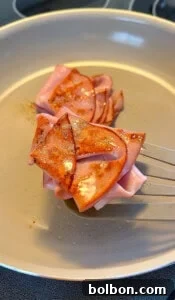 A close-up of sliced bologna being fried in a pan, with some edges browned and a spatula lifting one slice—perfect for adding to your low carb mortadella wraps.