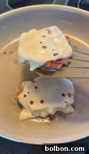 A spatula lifts a cooked patty topped with melted Swiss cheese and ham from a frying pan, while another similar patty is still cooking—perfect for enjoying with low carb mortadella wraps.