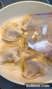 A hand pours water from a measuring cup into a skillet filled with Viral Blanket Dumplings, steaming or cooking these trendy potstickers to perfection.