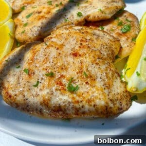 Grilled Lemon Chicken breasts garnished with chopped herbs, served on a white plate with lemon wedges on the side.