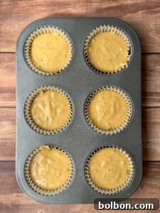 A six-cup muffin tray lined with paper cups, each filled with healthy sweet potato muffins batter, sits on a wooden surface, ready to be baked to perfection.