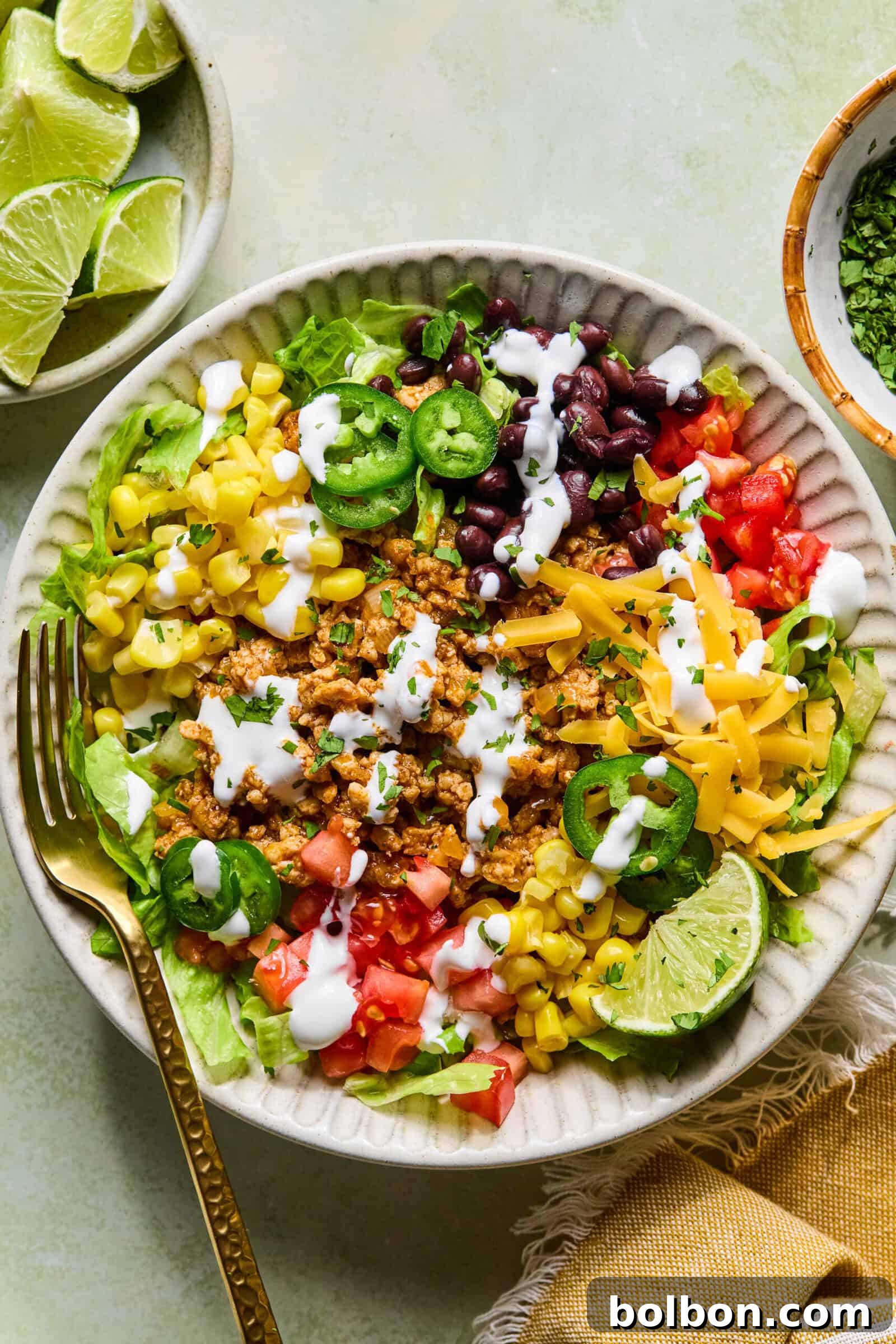 Hizli ve Dusuk Karbonhidratli Tavuklu Taco Kasesi 3 A top-down view of a delicious taco salad bowl loaded with ground meat, cheese, beans, corn, lettuce, and tomatoes, ready to be eaten with a fork.