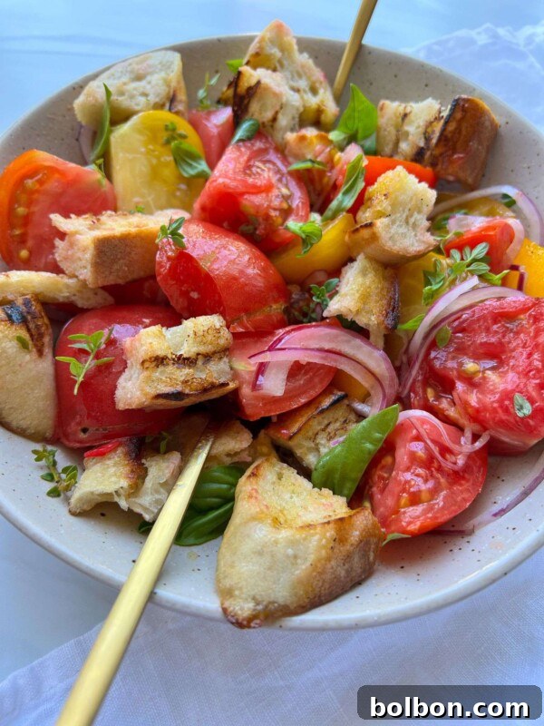 Pan con Tomate: Authentic Spanish Tomato Bread Recipe & How to Make It 5 A bowl of Panzanella Salad with colorful tomato wedges, toasted bread chunks, sliced red onions, basil leaves, and a light dressing is served with two gold forks.