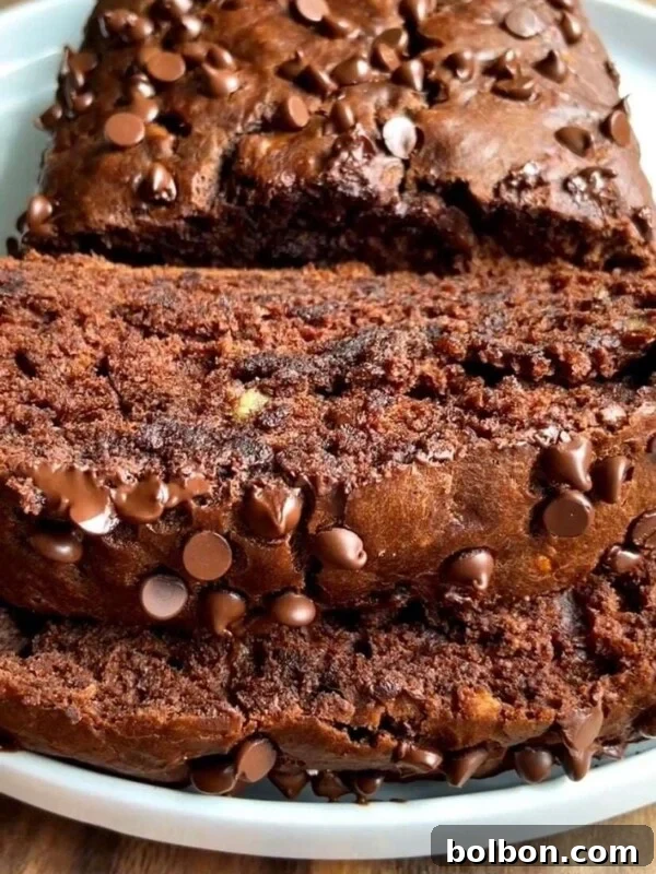 Close-up of thick slices of moist chocolate banana bread recipe topped with chocolate chips, displayed on a white plate. The bread looks rich, dense, and studded with chocolate chips throughout.
