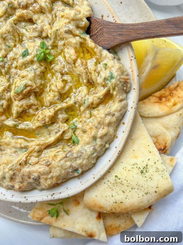 Fresh & Easy Mediterranean Bread Dipping Oil Recipe 6 A bowl of creamy baba ghanoush, made from a classic Baba Ghanoush Recipe, topped with herbs and olive oil, served with pita bread slices and a lemon wedge on a plate.