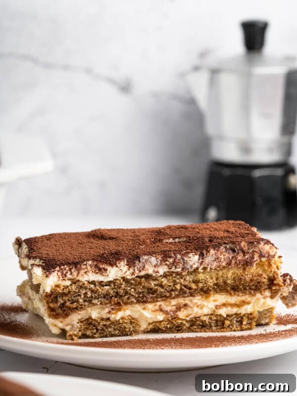 A slice of tiramisu on a white plate, with layers of coffee-soaked ladyfingers and creamy mascarpone, dusted with cocoa powder.