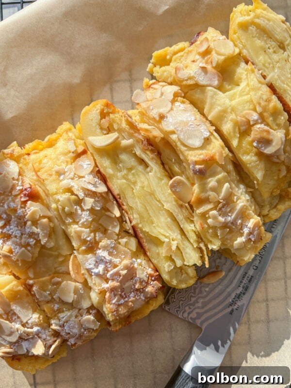 A close-up view of a sliced almond-topped pastry, dusted with powdered sugar.