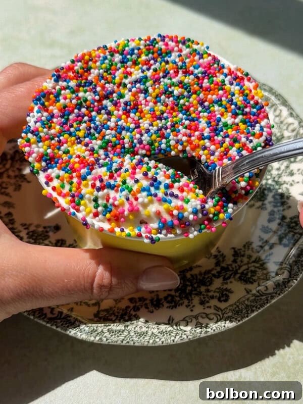 A person holds a cup of ice cream covered in colorful round sprinkles, resembling the look of a Viral Dot Cake.