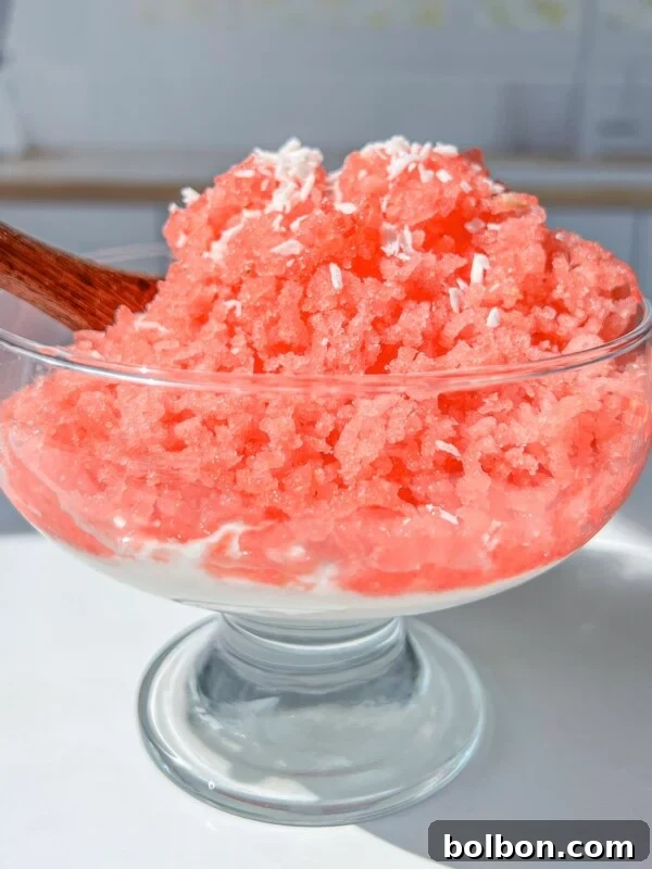 A glass dessert bowl filled with bright pink shaved ice topped with shredded coconut.