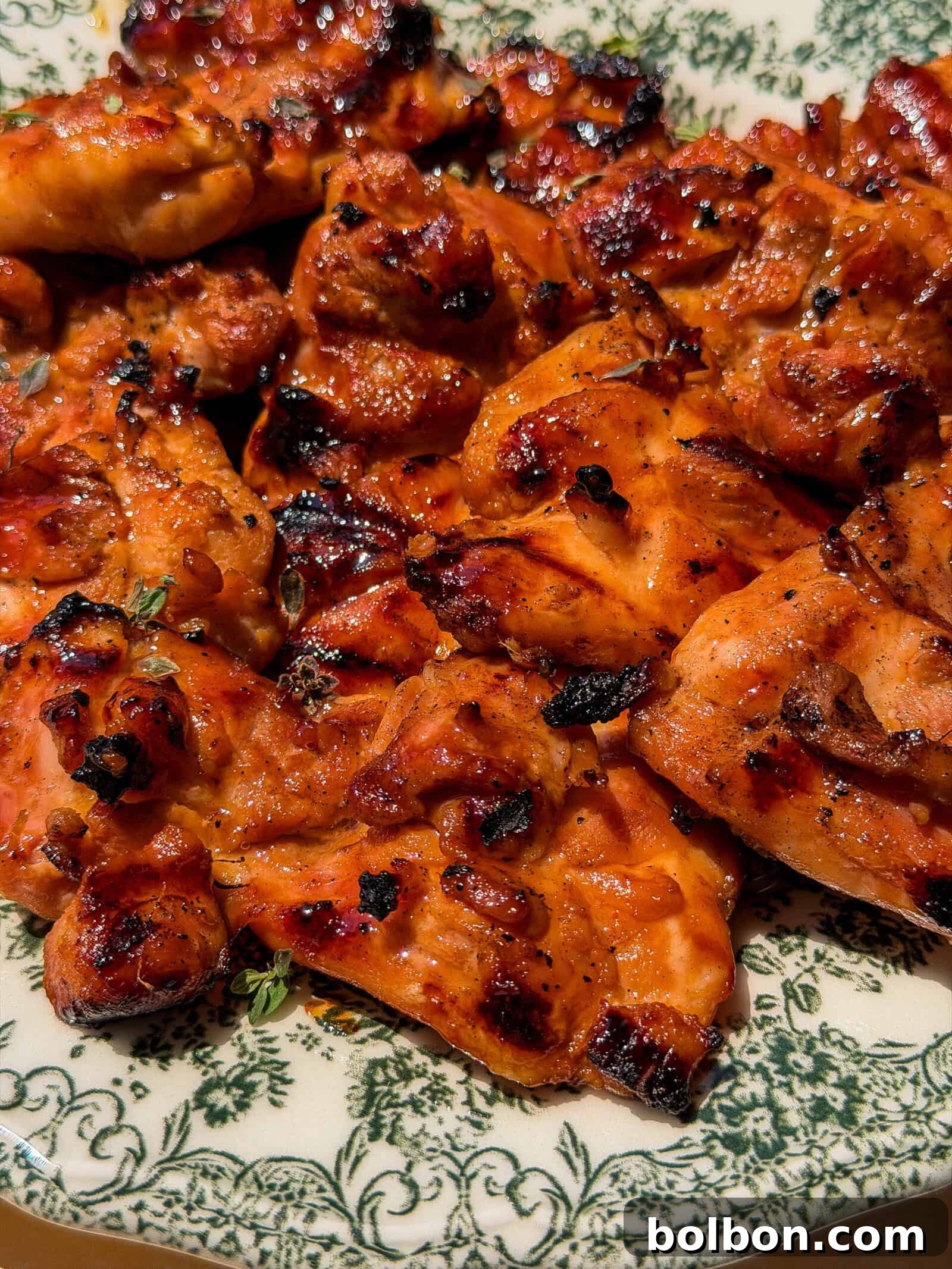 A close-up of grilled, charred chicken pieces with a reddish glaze served on a floral-patterned plate—perfect for pairing with a refreshing Viral Melon Ice Cream (2 Ingredients) dessert.