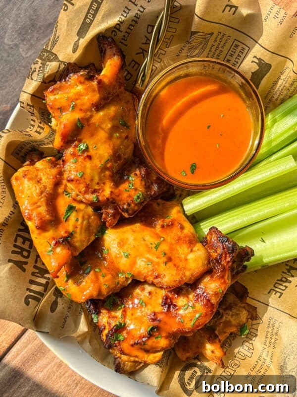 A plate of saucy grilled chicken wings with fresh celery sticks and a bowl of orange dipping sauce.