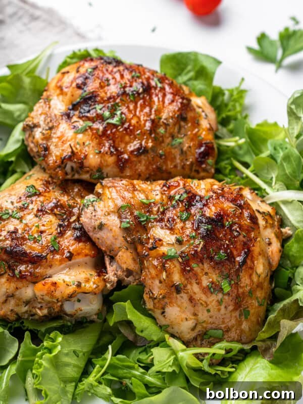 Grilled chicken thighs with a golden, crispy skin are garnished with herbs and served on leafy greens.