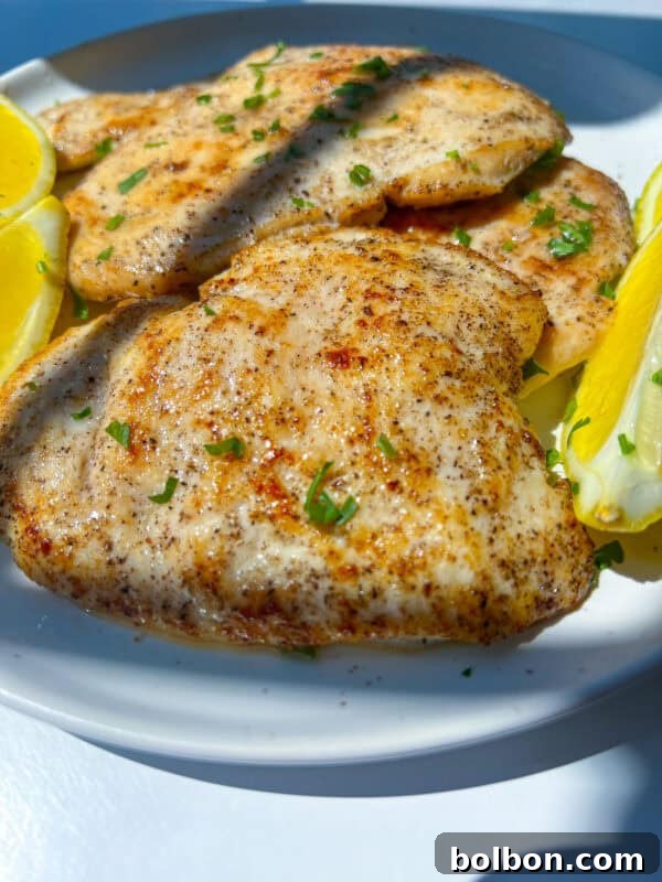 Grilled Lemon Chicken breasts garnished with chopped herbs, served on a white plate with lemon wedges.