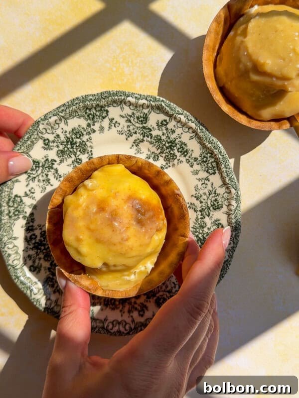 A person holds a vintage plate with a baked tart topped with melted cheese, reminiscent of flavors found in classic chicken marinades. Another tart sits on the table nearby, both lit by sunlight and shadow patterns.