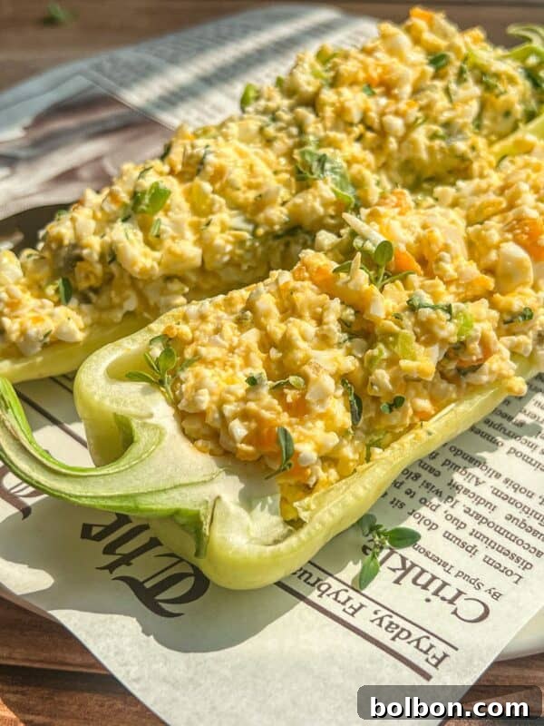 Two halved green bell peppers filled with a creamy egg salad mixture, garnished with fresh herbs.