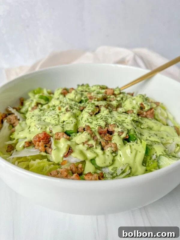 A white bowl filled with a green salad topped with crumbled meat and drizzled with a creamy green dressing.