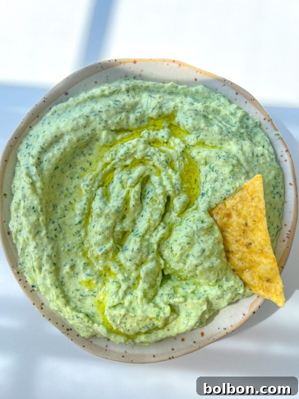 A bowl of creamy Green Goddess Dip with a single tortilla chip dipped in.