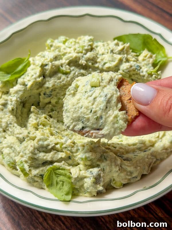 Hand dipping a chip into creamy green herb dip