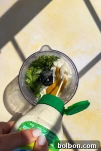 Hand pouring dressing into blender with herbs and sauce