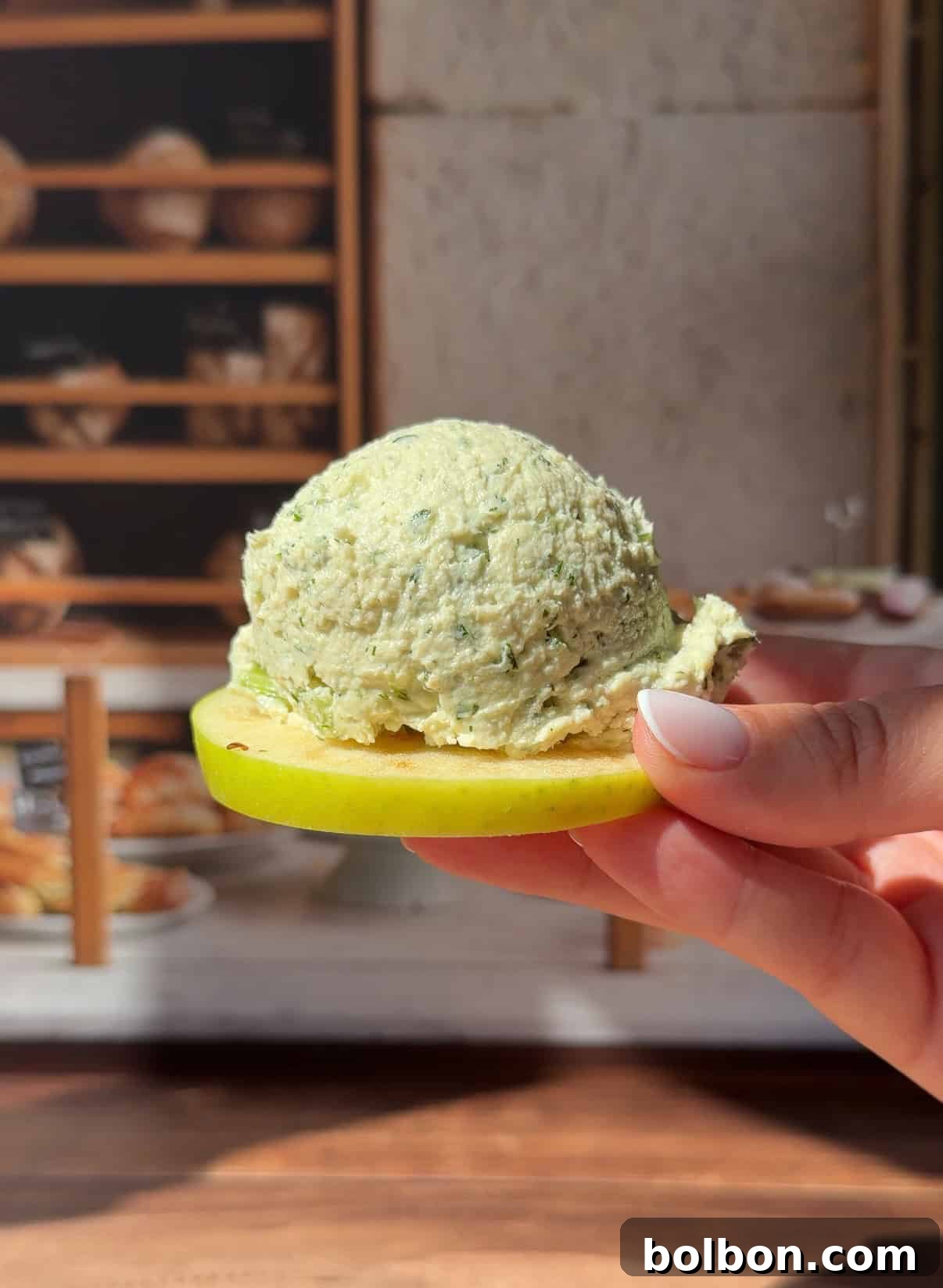 Hand holding herb cheese scoop on fresh apple slice