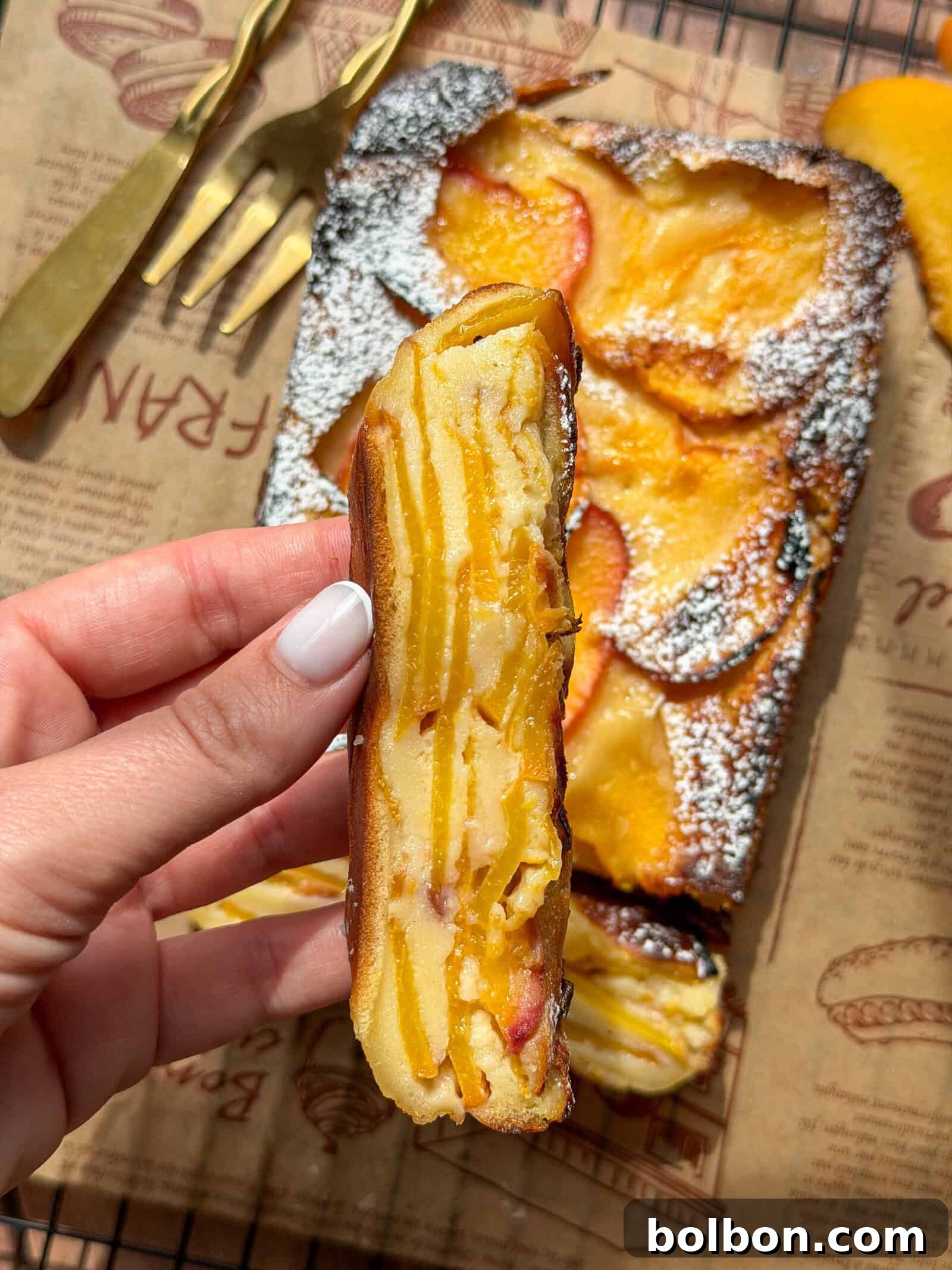 Invisible Peach Cake Recipe: Thin-Sliced Peach Dessert 4 Hand holding a slice of peach cake dusted with powdered sugar