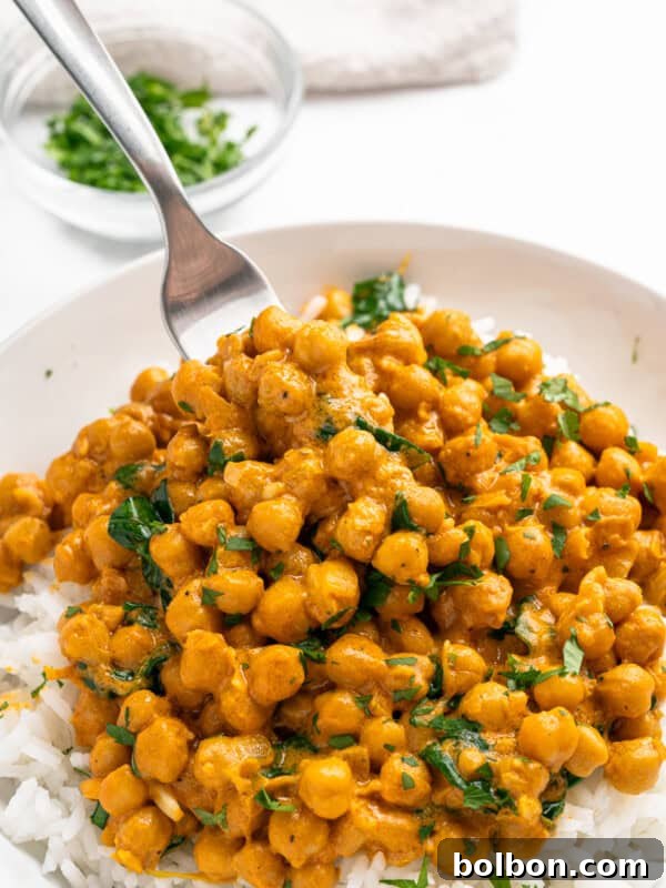 Creamy Butter Chicken Beans: Indian-Spiced Bean Curry 5 A plate of white rice topped with chickpea curry garnished with chopped cilantro