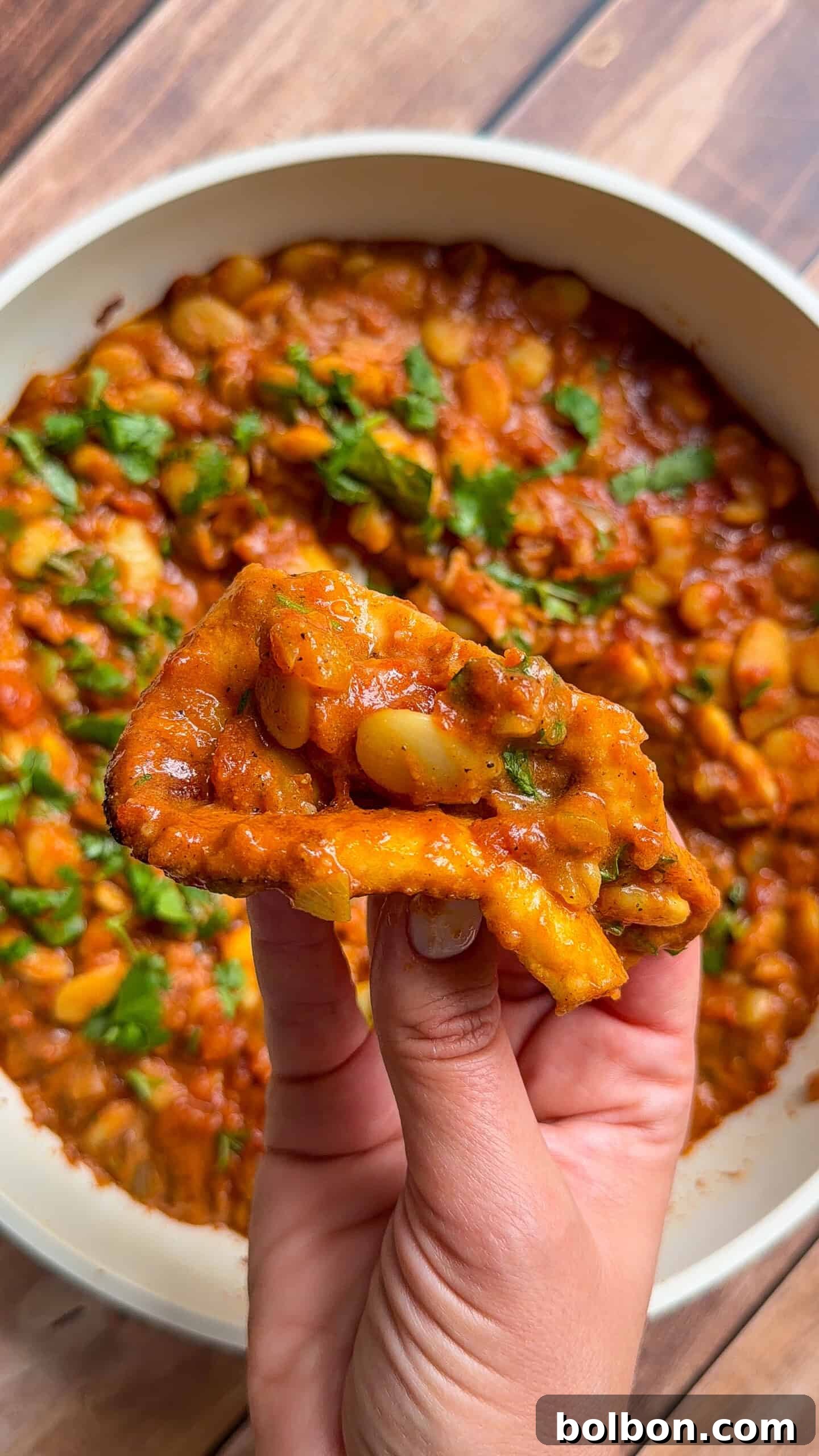 Creamy Butter Chicken Beans: Indian-Spiced Bean Curry 3 Hand holding fried bread dipped in butter chicken beans