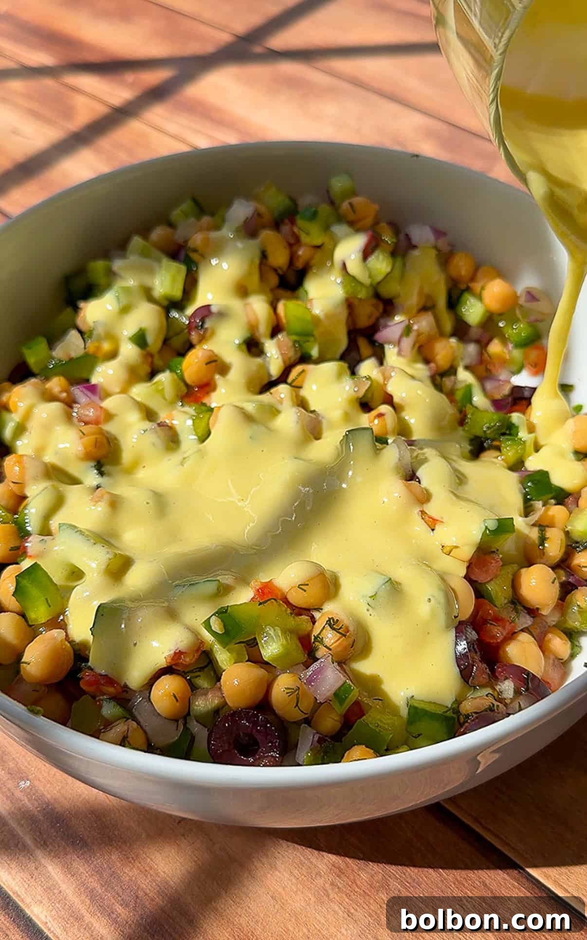 Creamy dressing being poured over chickpea salad bowl