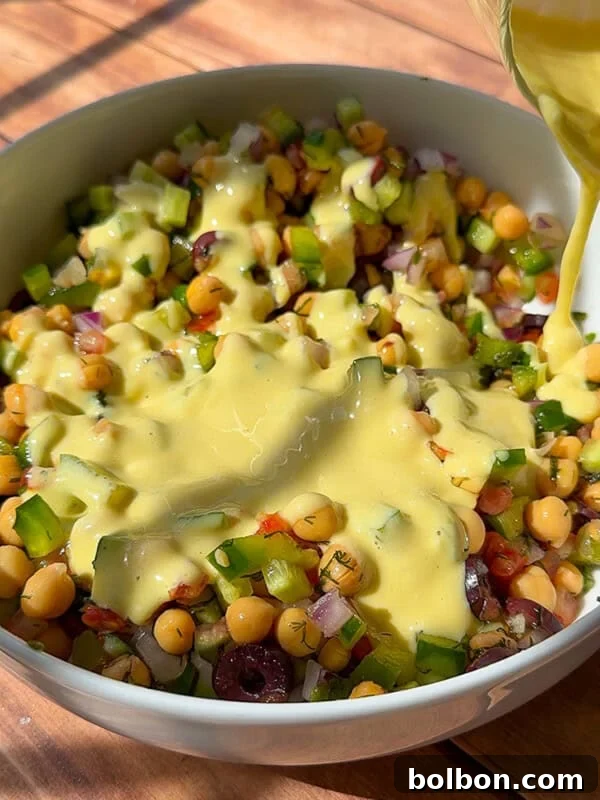 Creamy dressing being poured over chickpea salad bowl